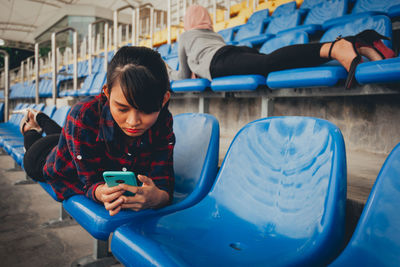 Young woman using mobile phone while sitting on laptop