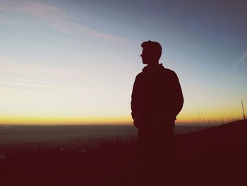 Silhouette man standing on field against clear sky at sunset