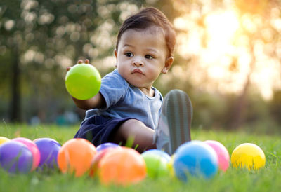 Cute baby boy playing with colorful balls on grassy field at park