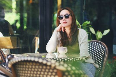 Portrait of young woman wearing sunglasses while sitting at outdoor cafe