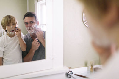 Father and son shaving while reflecting in mirror