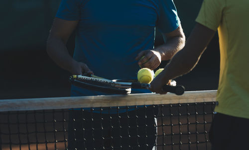 Midsection of tennis players standing at net on court