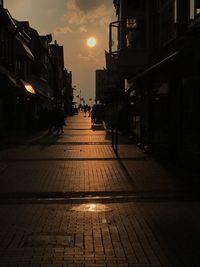 Empty footpath amidst buildings in city at sunset