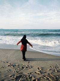 Rear view of man standing on beach against sky