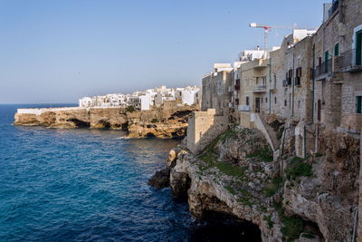 Buildings by sea against clear blue sky