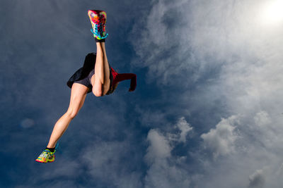 Low angle view of woman jumping against sky
