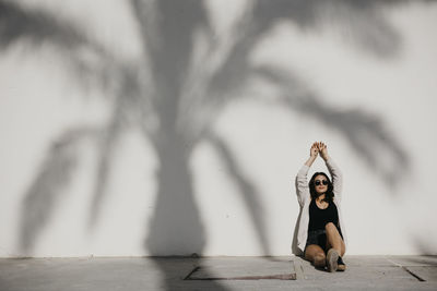 Full length of woman with arms raised against wall