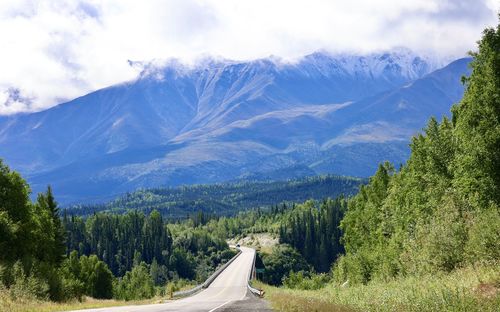 Road amidst trees and mountains against sky