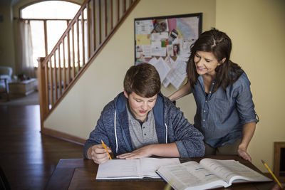 Smiling mother looking at son studying on table