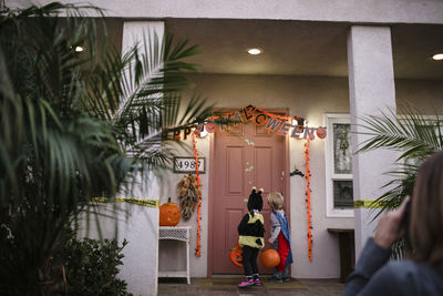 Rear view of siblings wearing costumes while trick or treating on porch during halloween