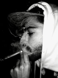 Close-up of man smoking cigarette against black background