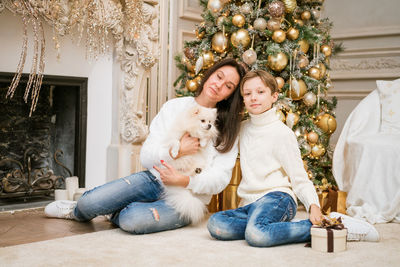 Happy family, mom and son. they are sitting near a christmas tree with a dog.