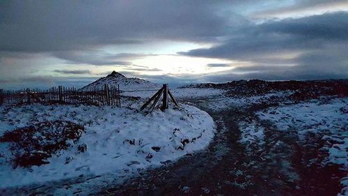 Snow covered landscape against cloudy sky