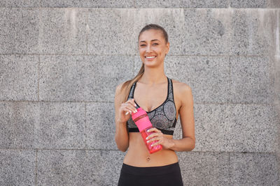 Portrait of a smiling young woman standing against wall