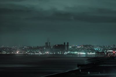 Illuminated cityscape by sea against sky at night