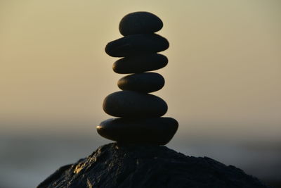 Stack of stones on rock against sky during sunset