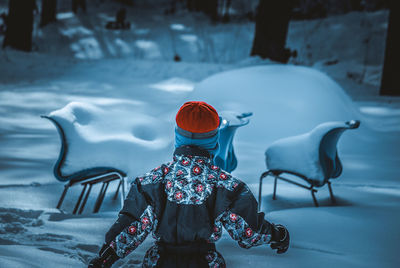 Rear view of boy standing at snow covered park during winter