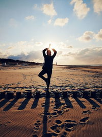 Full length of woman doing yoga at beach against cloudy sky during sunset