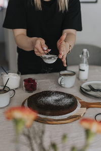 Woman putting powdered sugar on freshly baked chocolate cake