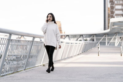 Full length portrait of young woman standing on railing
