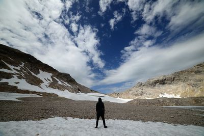 Rear view of man standing on snowcapped mountain against sky