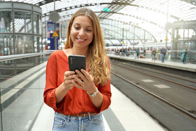 Smiling attractive brazilian traveler passenger buys ticket online with smartphone in train station.