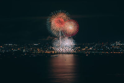 Firework display over illuminated city against sky at night