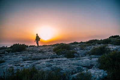 Silhouette man standing on rock against sky during sunset