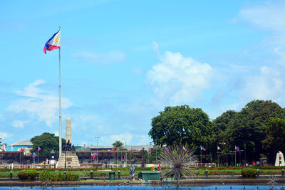 Red flag by trees against sky in city