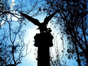 Low angle view of silhouette statue against bare trees