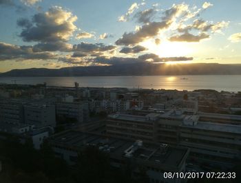 Cityscape by sea against sky during sunset