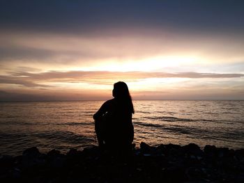 Rear view of silhouette woman sitting on rock at sunset