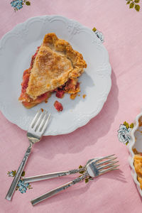 Single slice of rhubarb pie on white plate, pink tablecloth with blue roses