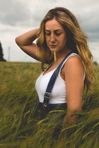 Close-up of young woman with grass in mouth standing on field against sky