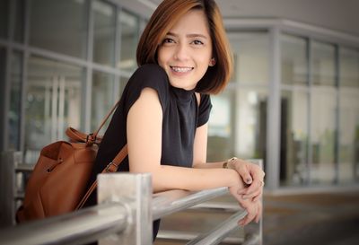 Portrait of young woman smiling while leaning on railing