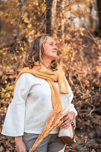 Woman looking away while standing on tree during autumn