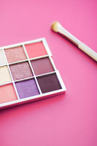 Close-up of multi colored beauty product and make-up brush against pink background