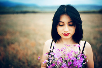 Close-up of young woman with flowers on field