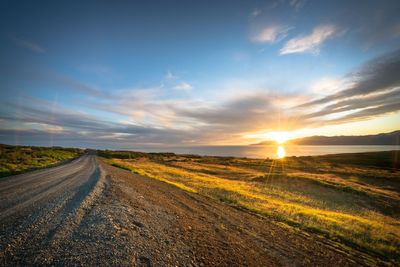 Road amidst field against sky during sunset