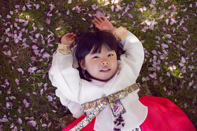 Korean girl child in a national costume lies on the back in a garden with cherry blossoms in spring