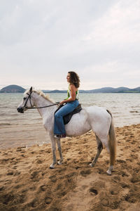 Smiling young woman riding horse at waterfront