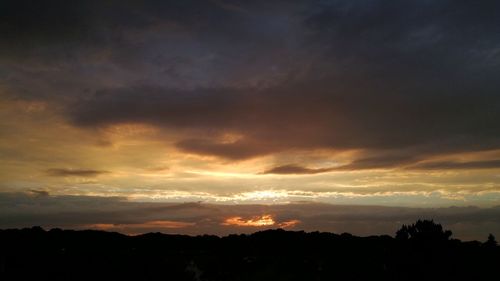 Silhouette trees against dramatic sky during sunset