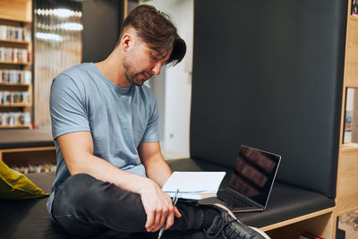 Student learning in university library. young man reading his notes. man using computer to learn