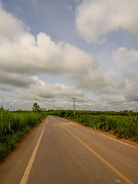 Empty road amidst field against sky