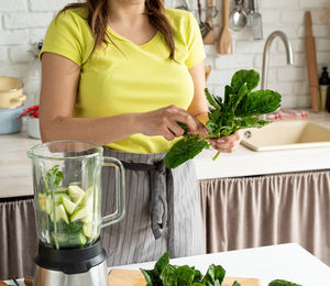 Healthy eating and dieting. young brunette woman making green smoothie at home kitchen