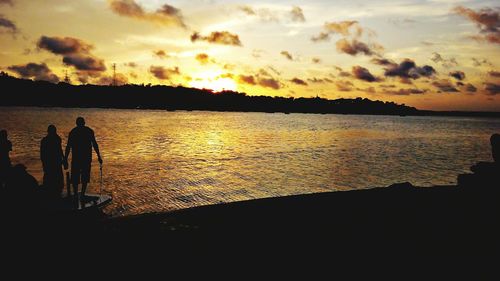 Silhouette people standing by sea against sky during sunset