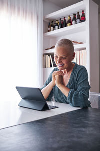Smiling woman looking at digital tablet while sitting in living room