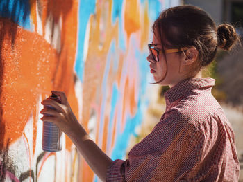 Side view of young woman spraying graffiti on wall