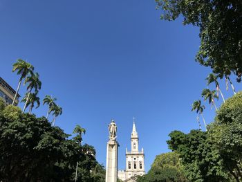 Low angle view of trees and building against clear blue sky