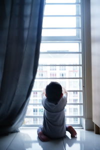 Rear view of a man looking through window at home